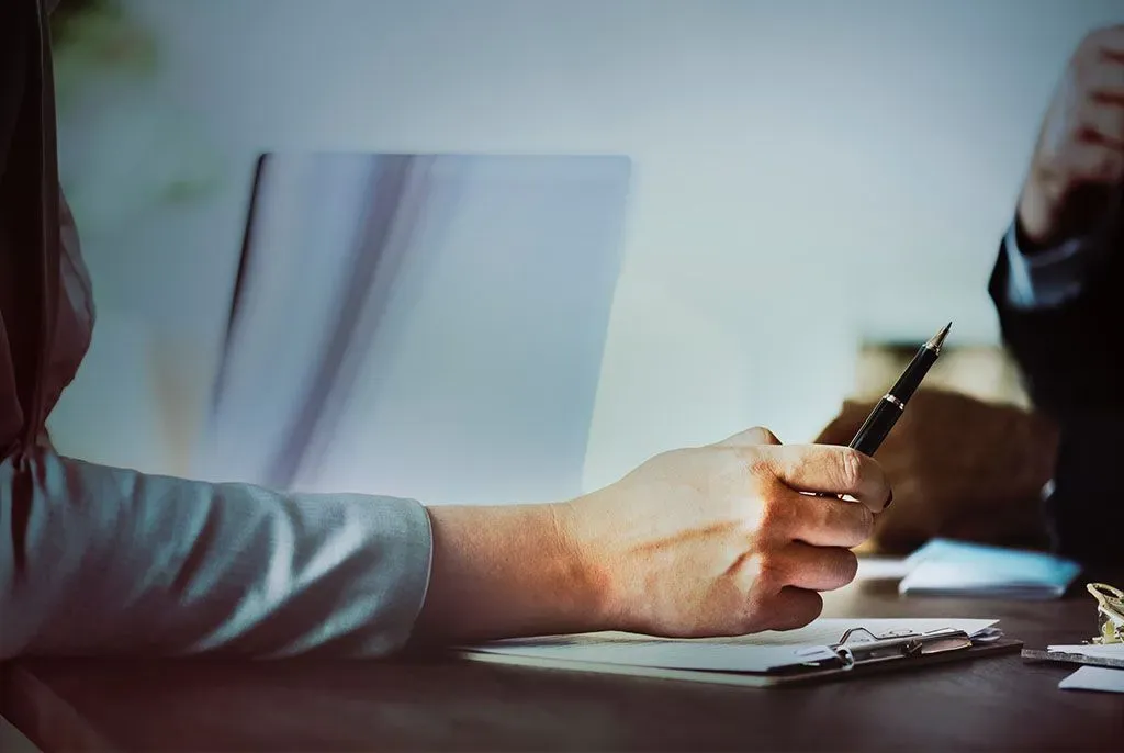 Personne rédigeant un avis de décès avec un stylo lors de démarches d'obsèques.