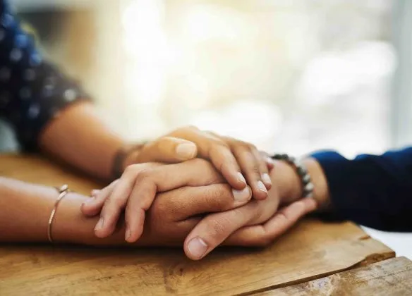 Mains enlacées sur une table en bois symbolisant le soutien et le réconfort.