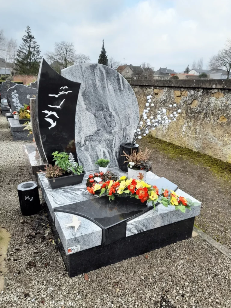 Petit monument cinéraire en granit gris et noir fleuri dans un cimetière.