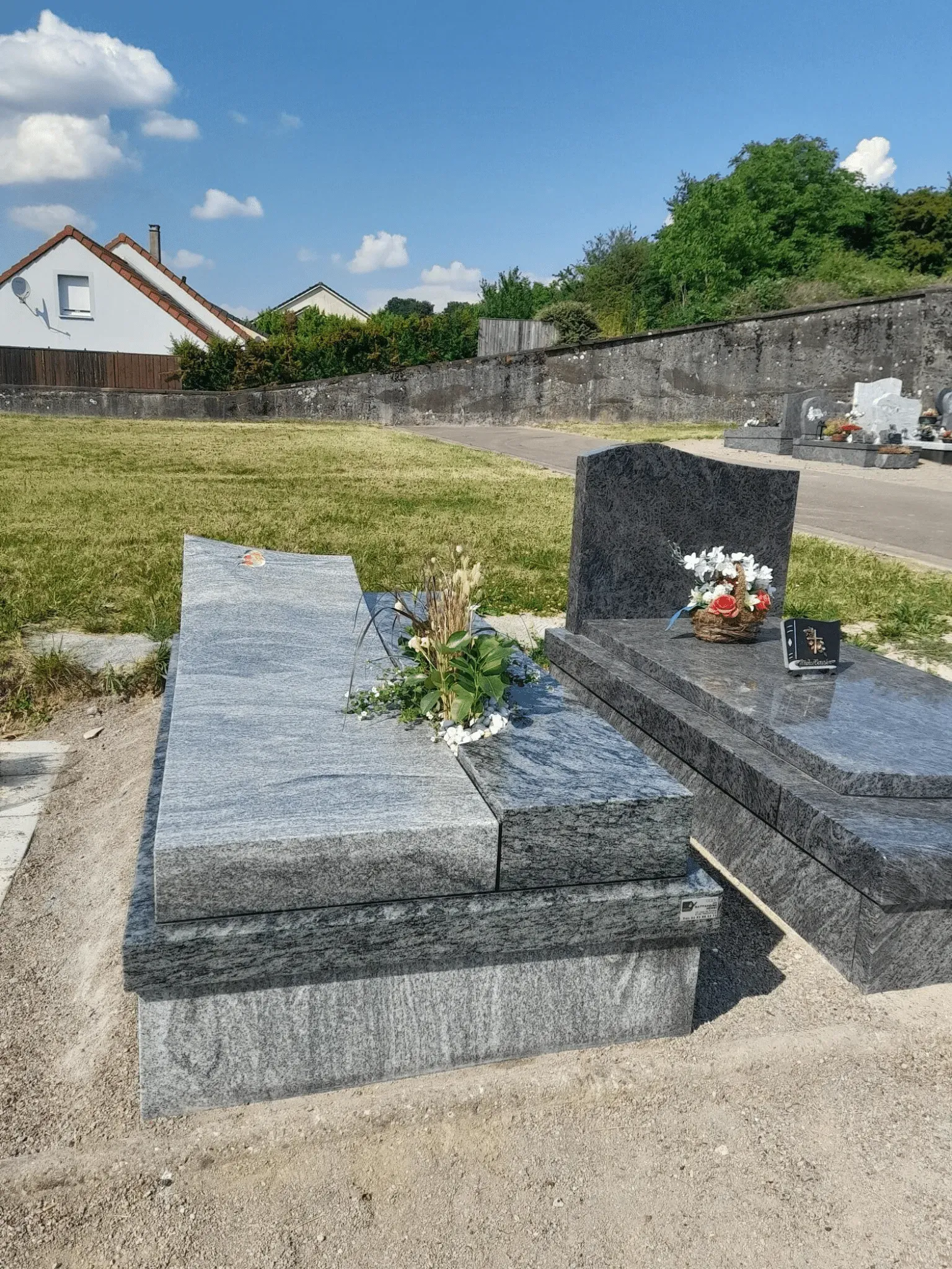 Monument funéraire moderne en granit gris moucheté surmonté de fleurs.