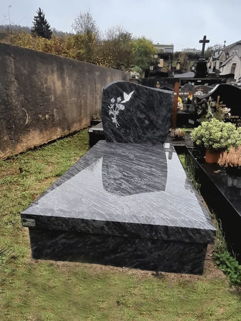 Sépulture en granit gris nuancé surmontée d'une croix dorée gravée.