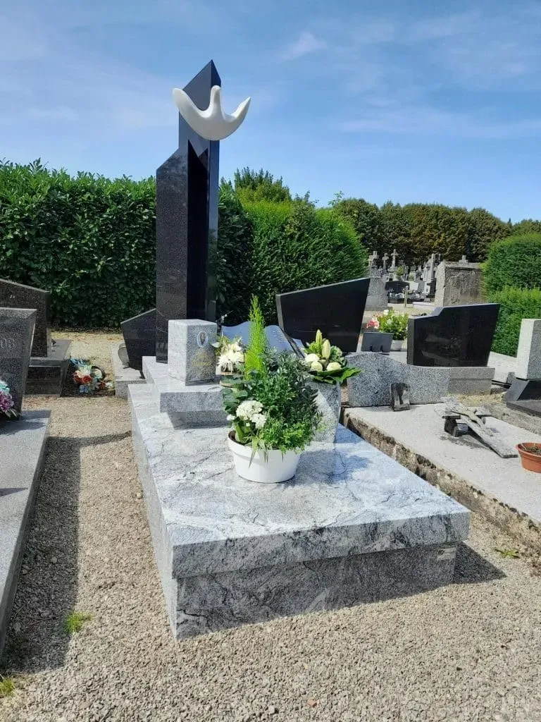 Monument funéraire moderne en granit gris avec stèle sculptée d'une colombe.